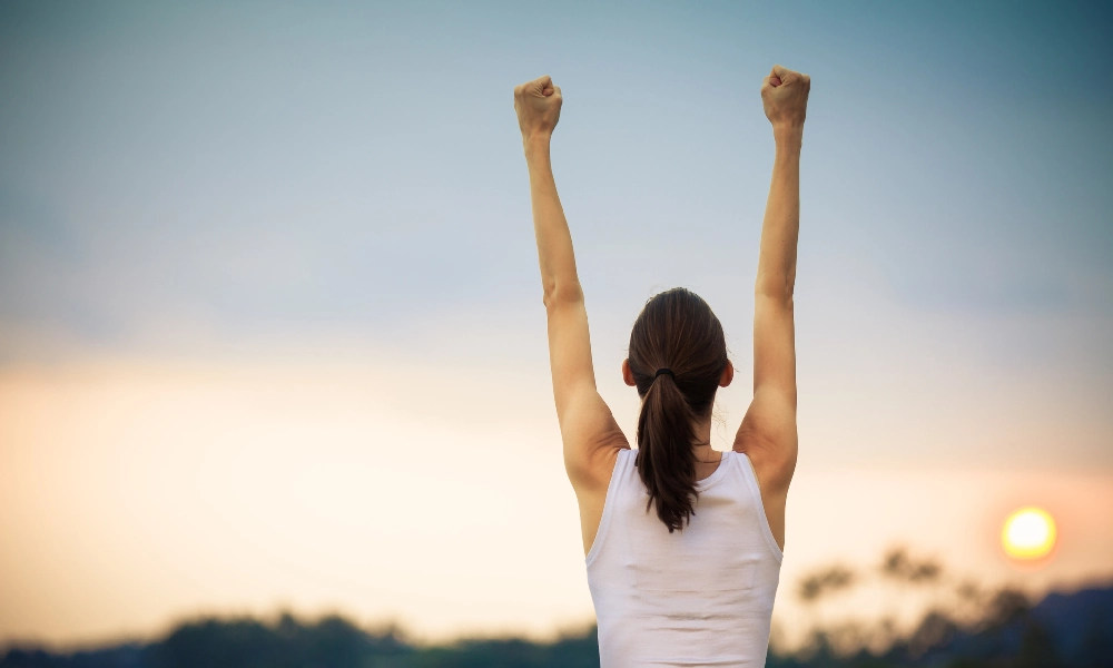 دختری جوان که به نشانه ی پیروزی دستانش را مشت کرده است | افزایش عزت نفس