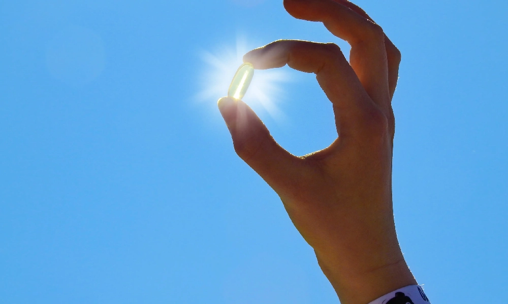 فردی که یک قرص ویتامین دی را روبروی نور خورشید قرار داده است | علائم کمبود ویتامین دی