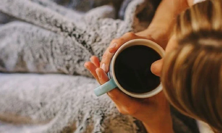 کاهش تپش قلب ناشی از قهوه | دختر جوانی که روی تختش در حال خوردن قهوه است